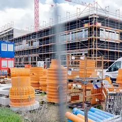 Baustellenansicht des Sutter-Neubaus in Emmendingen mit eingerüstetem Gebäude, bunten Baucontainern und gelagertem Baumaterial im Vordergrund.