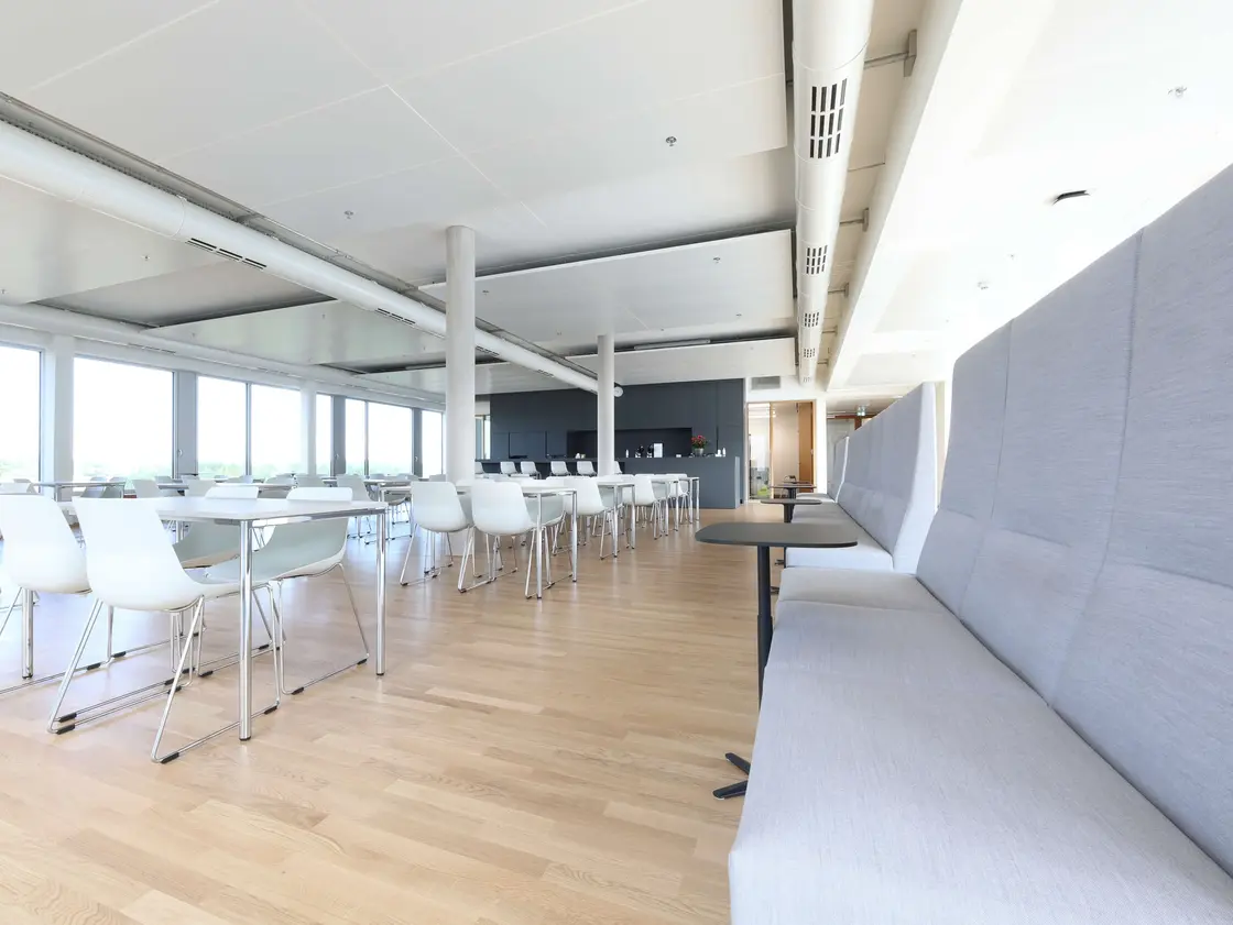 Heller, moderner Sozialraum bei Sutter Medizintechnik mit langen grauen Sitzbänken, weißen Stühlen, Tischen und großer Fensterfront.