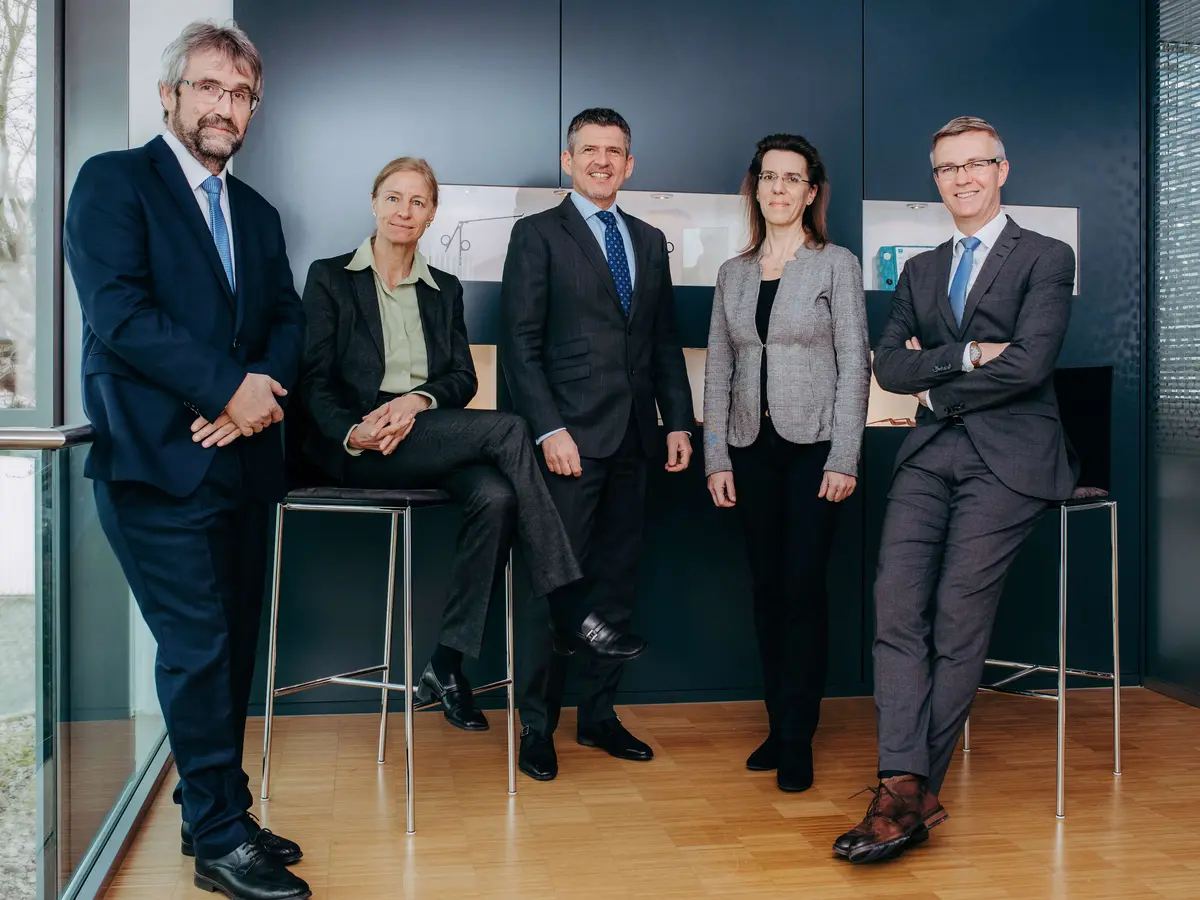 Fünf Mitglieder des Führungsteams von Sutter Medizintechnik stehen gemeinsam in Businesskleidung vor einer dunklen Wand – Symbol für Kompetenz, Zusammenarbeit und moderne Unternehmensführung