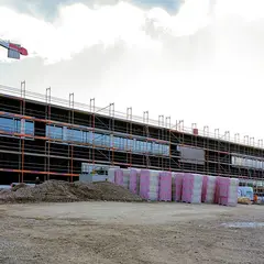 Ansicht des Neubaus der Sutter Medizintechnik GmbH mit eingerüsteter Fassade, Kran und Baumaterialien auf dem Baugelände während der Fassadenarbeiten.