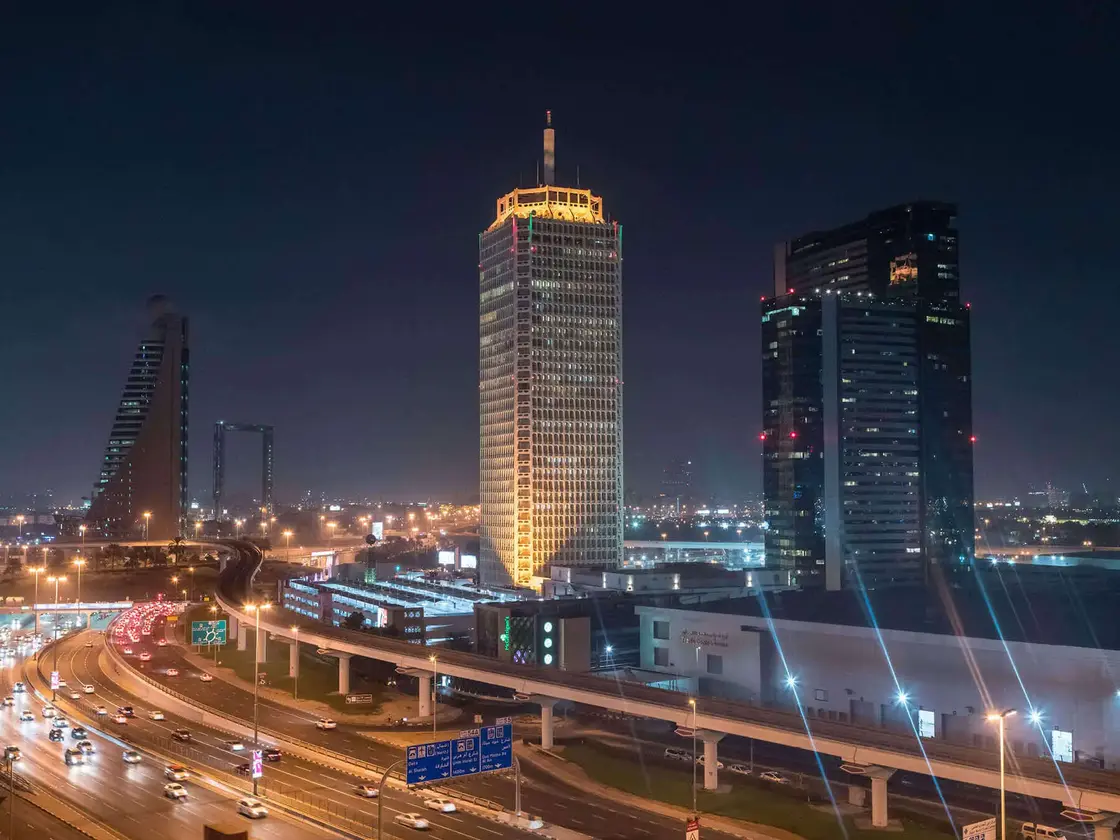 Nächtlicher Blick auf die Skyline von Dubai mit beleuchteten Hochhäusern und der Sheikh Zayed Road – modernes Stadtbild mit Verkehr und Architektur.