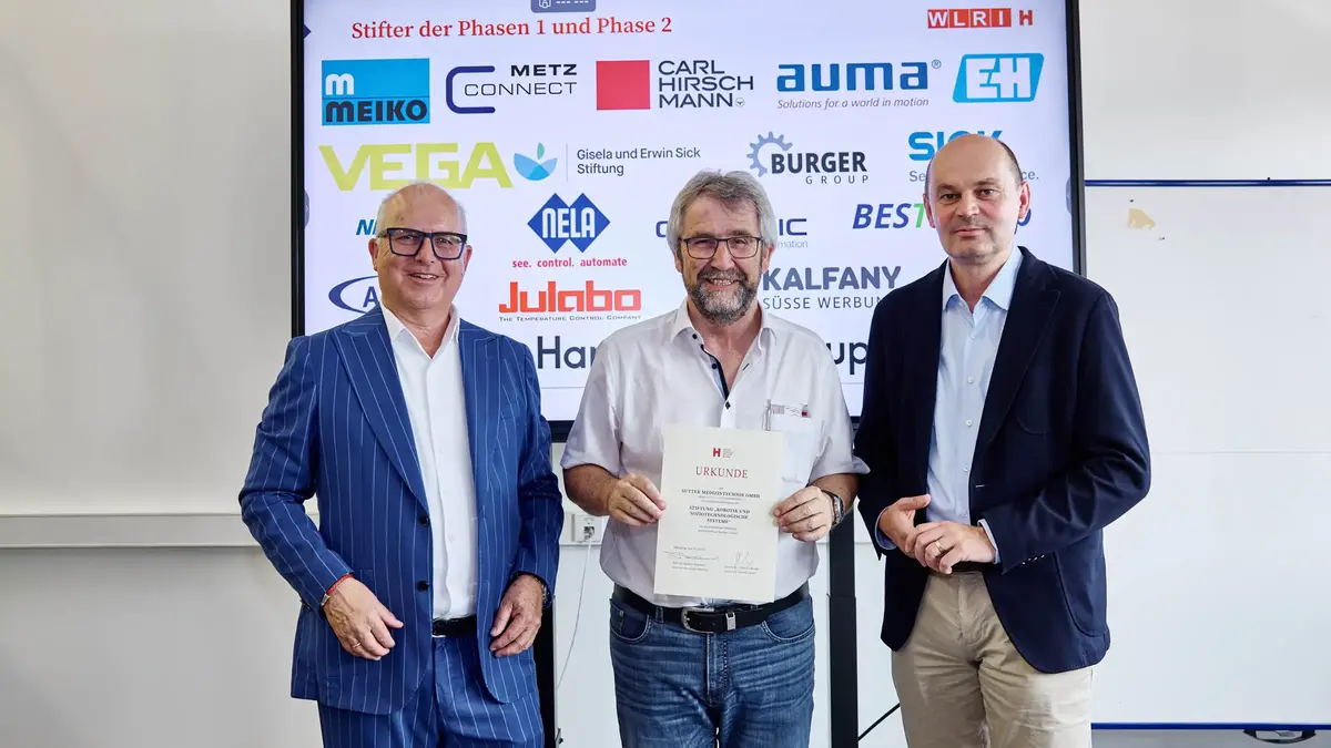 Drei Männer bei einer Urkundenübergabe vor einer Sponsorenwand am Robotiktag 2025; ein Vertreter von Sutter Medizintechnik hält die Urkunde der Hochschule Offenburg.
