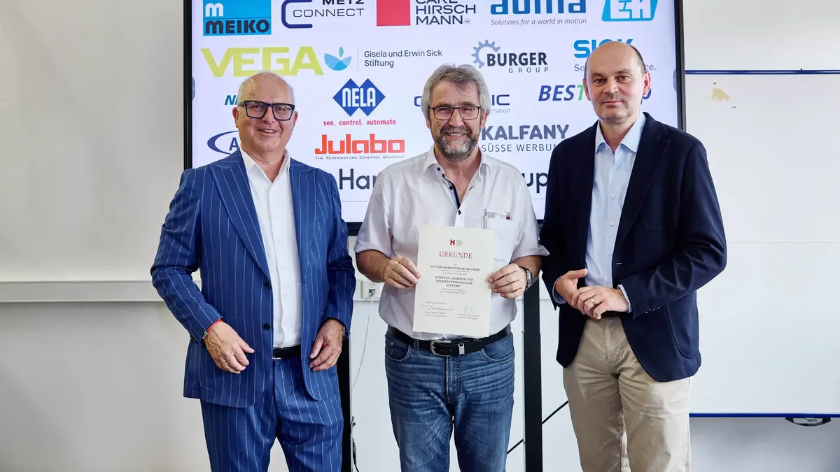 Drei Männer bei einer Urkundenübergabe vor einer Sponsorenwand am Robotiktag 2025; ein Vertreter von Sutter Medizintechnik hält die Urkunde der Hochschule Offenburg.