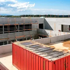 Innenhof des neuen Firmengebäudes der Sutter Medizintechnik GmbH im Rohbauzustand mit eingerüsteter Fassade, einem roten Baucontainer und Blick auf die umliegende Landschaft.