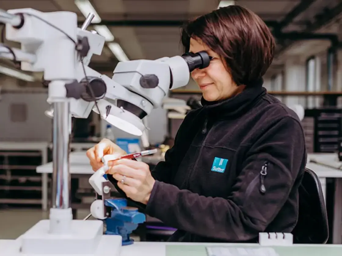 Mitarbeiterin von Sutter Medizintechnik arbeitet hochkonzentriert unter dem Mikroskop in der präzisen Montage von medizinischen Instrumenten