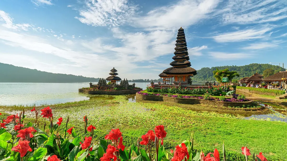 Pura Ulun Danu Temple on Lake Bratan in Bali with flowers, water, and blue sky.