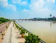 Ahmedabad riverfront with bridge, trees, promenade, and modern city skyline.