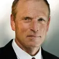 Prof. Dr. Kühnel im dunklen Anzug mit weißem Hemd und gestreifter Krawatte vor neutralem Hintergrund.