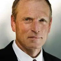 Prof. Dr. Kühnel im dunklen Anzug mit weißem Hemd und gestreifter Krawatte vor neutralem Hintergrund.