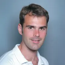 Dr. Hirt mit kurzem Haar und weißem Polohemd vor blauem Hintergrund.